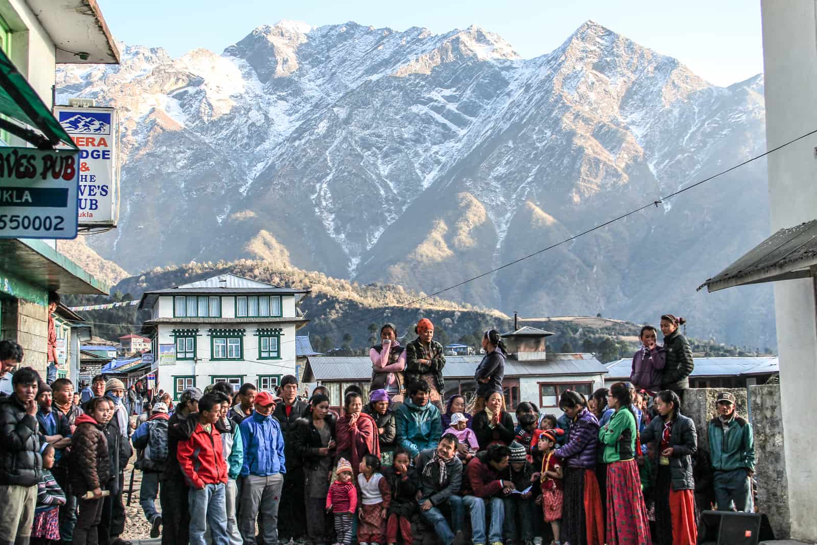 A group of Nepalese people gather in an open square in the town of Luka, based by high mountain ranges