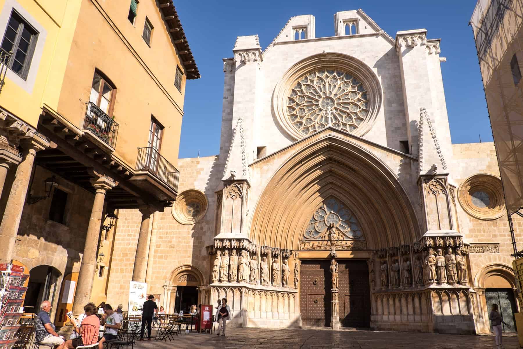 The white exterior of the Tarragona Cathedral of Tarragona on the site of the former Roman temple. On the left people are dining outside at a neighbouring restaurant