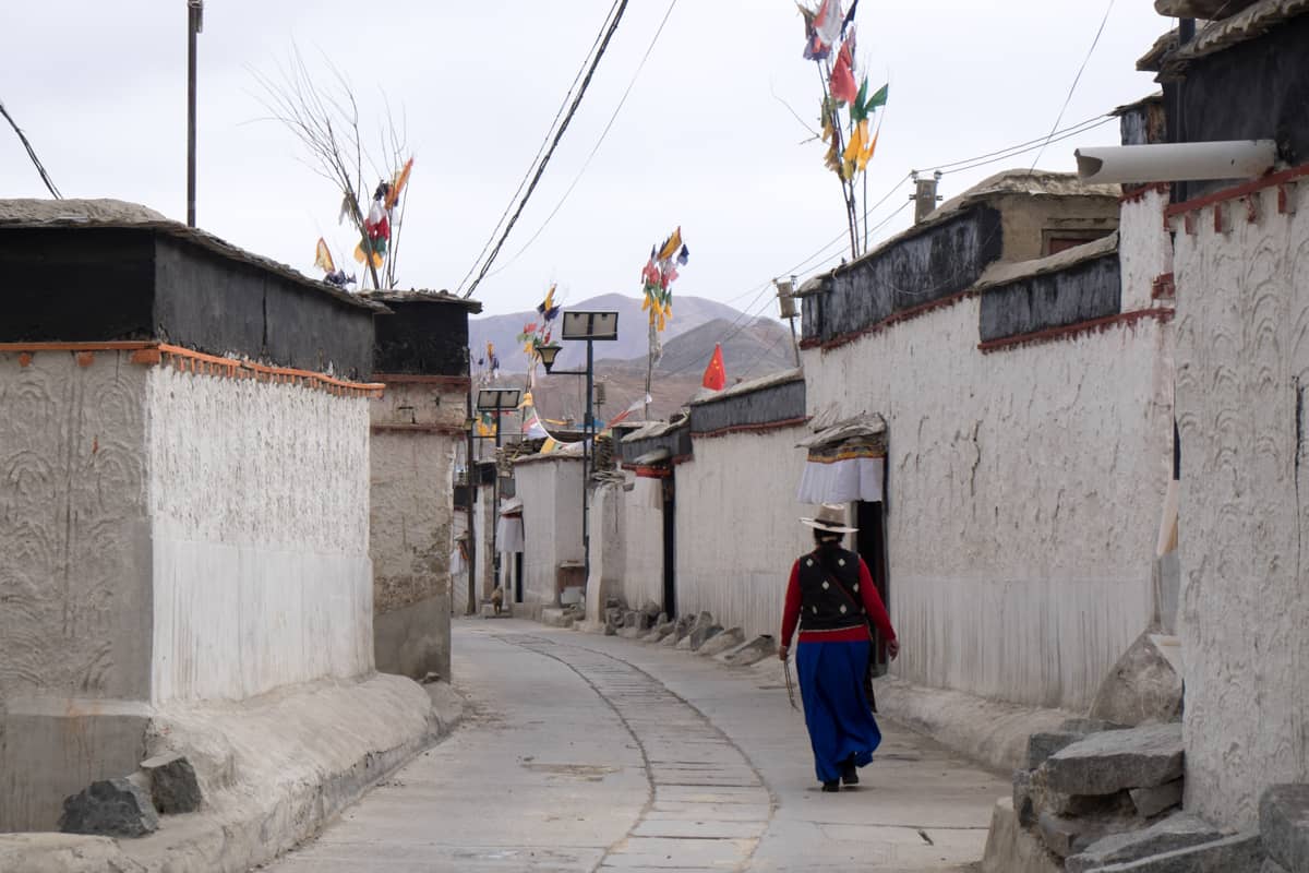 A Tibetan woman walks alongside traditional white houses of a village in Shigatse, Tibet