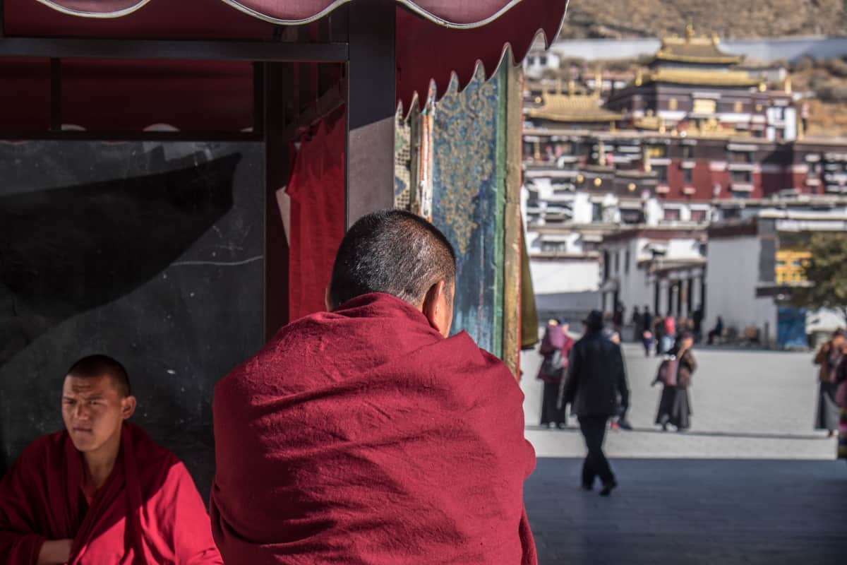 The back of a monk sitting outside the entrance to the Tashi Lhunpo Monastery in Shigatse, Tibet