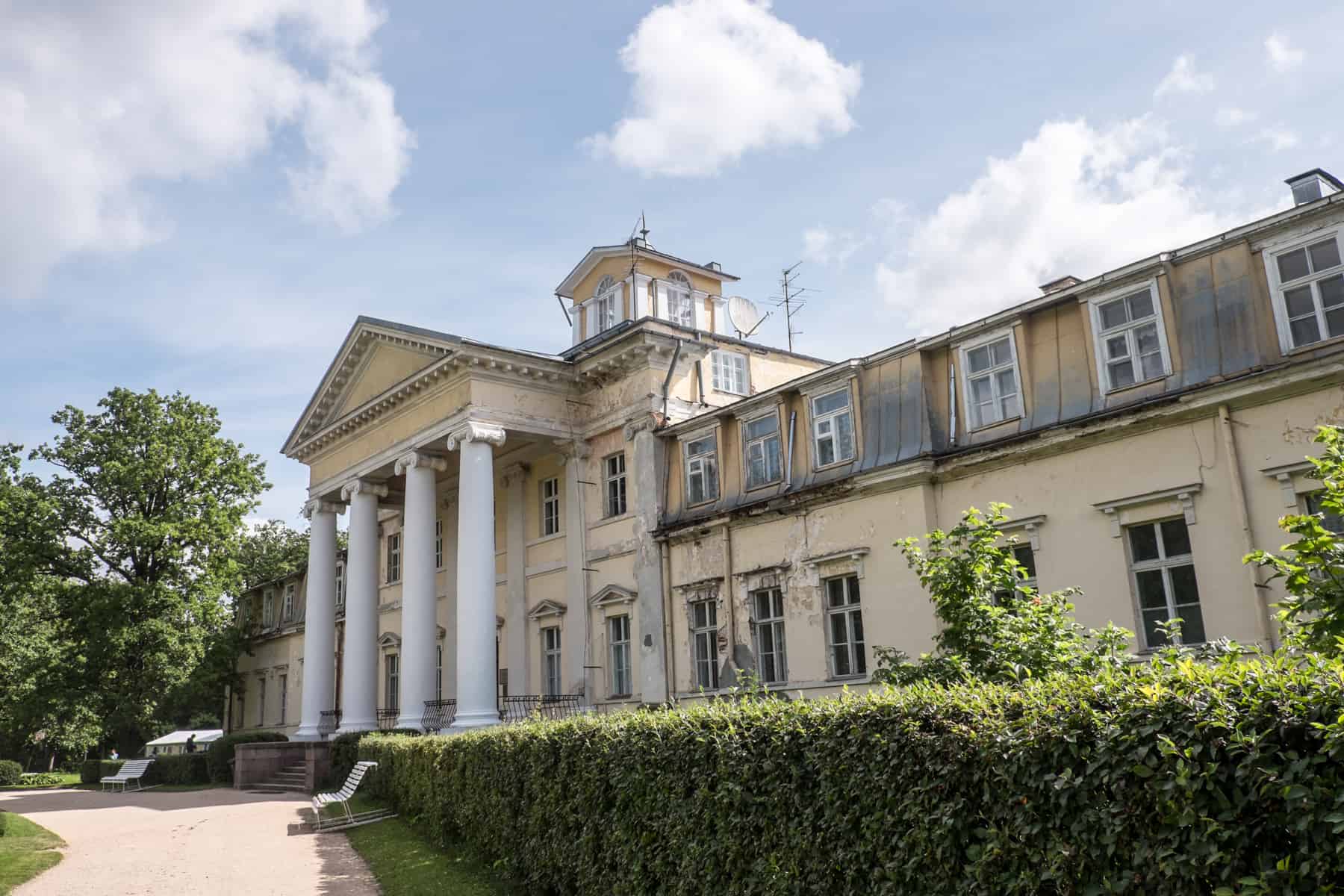 Krimulda Manor in Sigudla - a yellow neo-classical style building with white columns at the entrance, surrounded by manicured green hedges