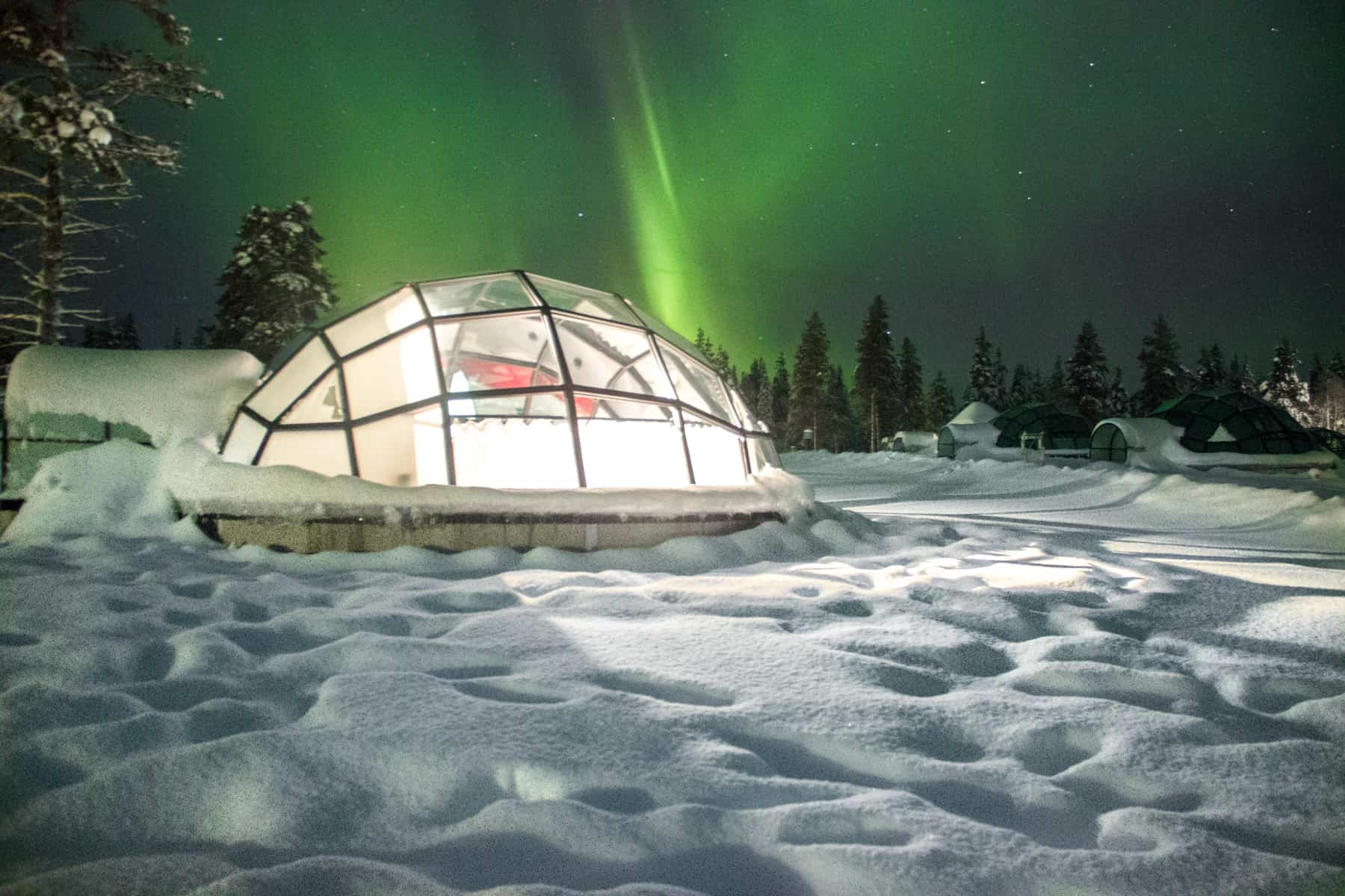 A glass igloo on white snow under the green northern lights in Finland Lapland