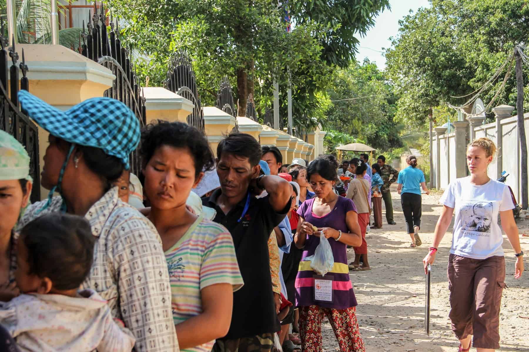 A Woman Volunteering in Cambodia, walks alongside a long queue of people