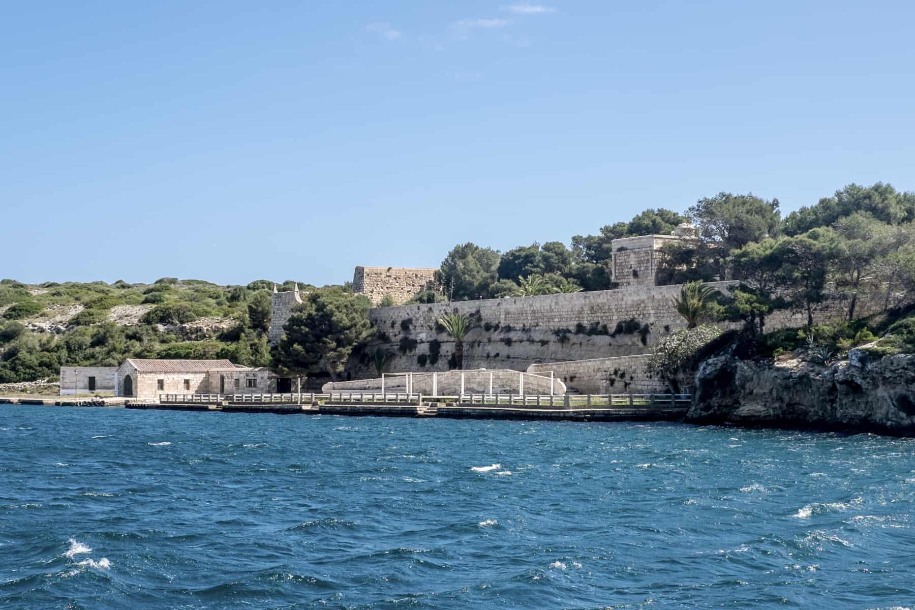 Old walls and defence structures on the blue ocean coastline of Menorca. 