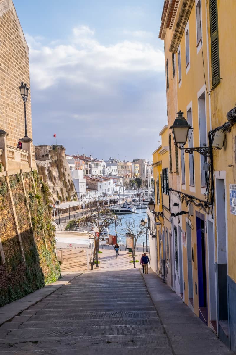 A view to the port of Ciutadella in Menorca from a street lined with yellow houses.