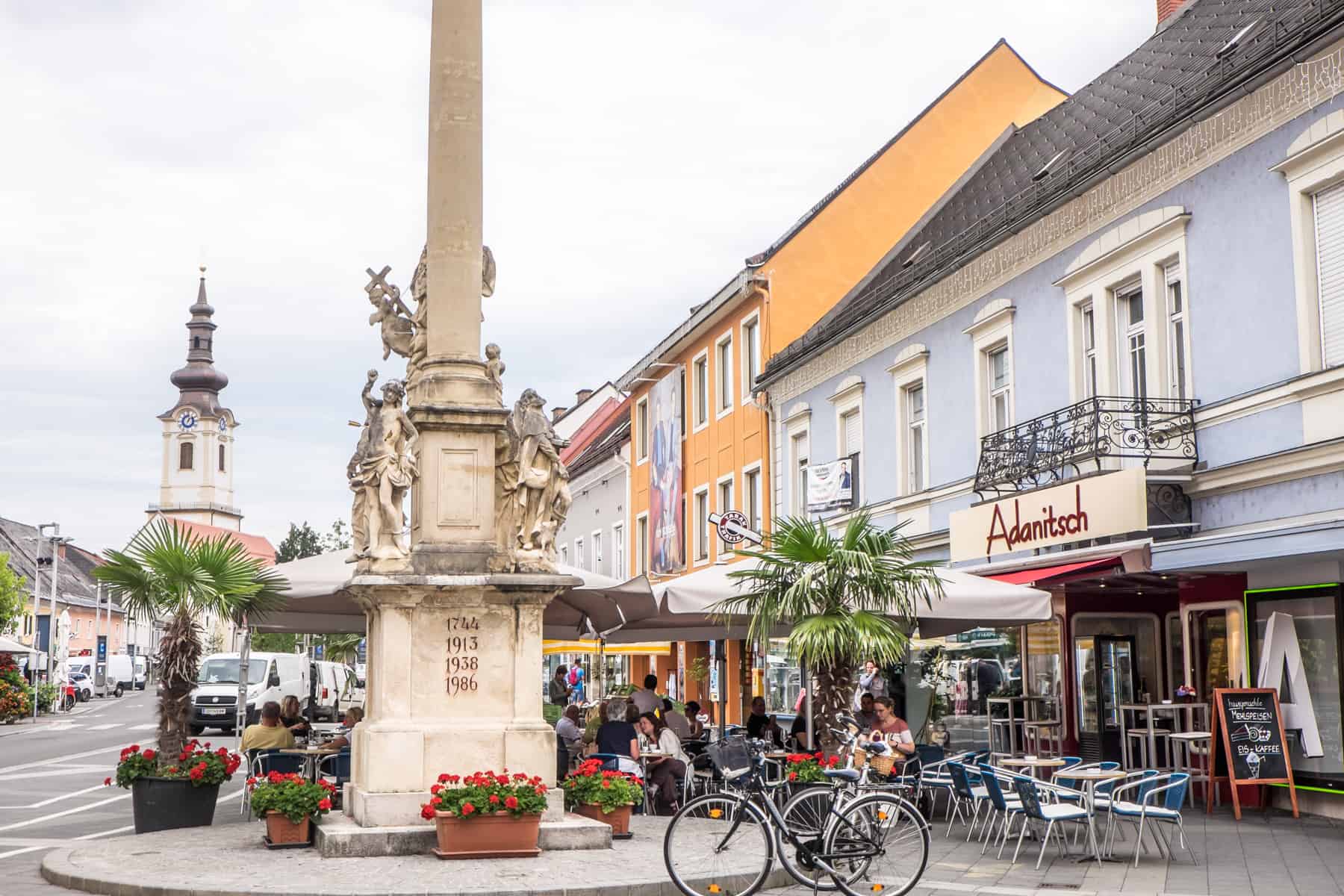 The beige column fountain and pastel blue building with a church in the background, in the town centre of Leibnitz, Austria