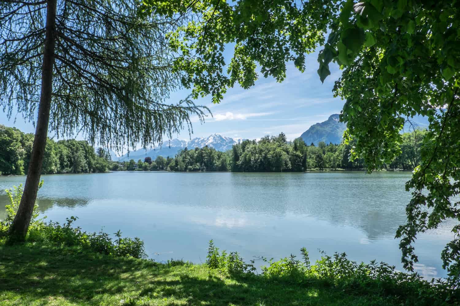 The shimmering blue, mountain backed, tree-lined Sound of Music Lake at Schloss Leopoldskron in Salzburg, Austria.
