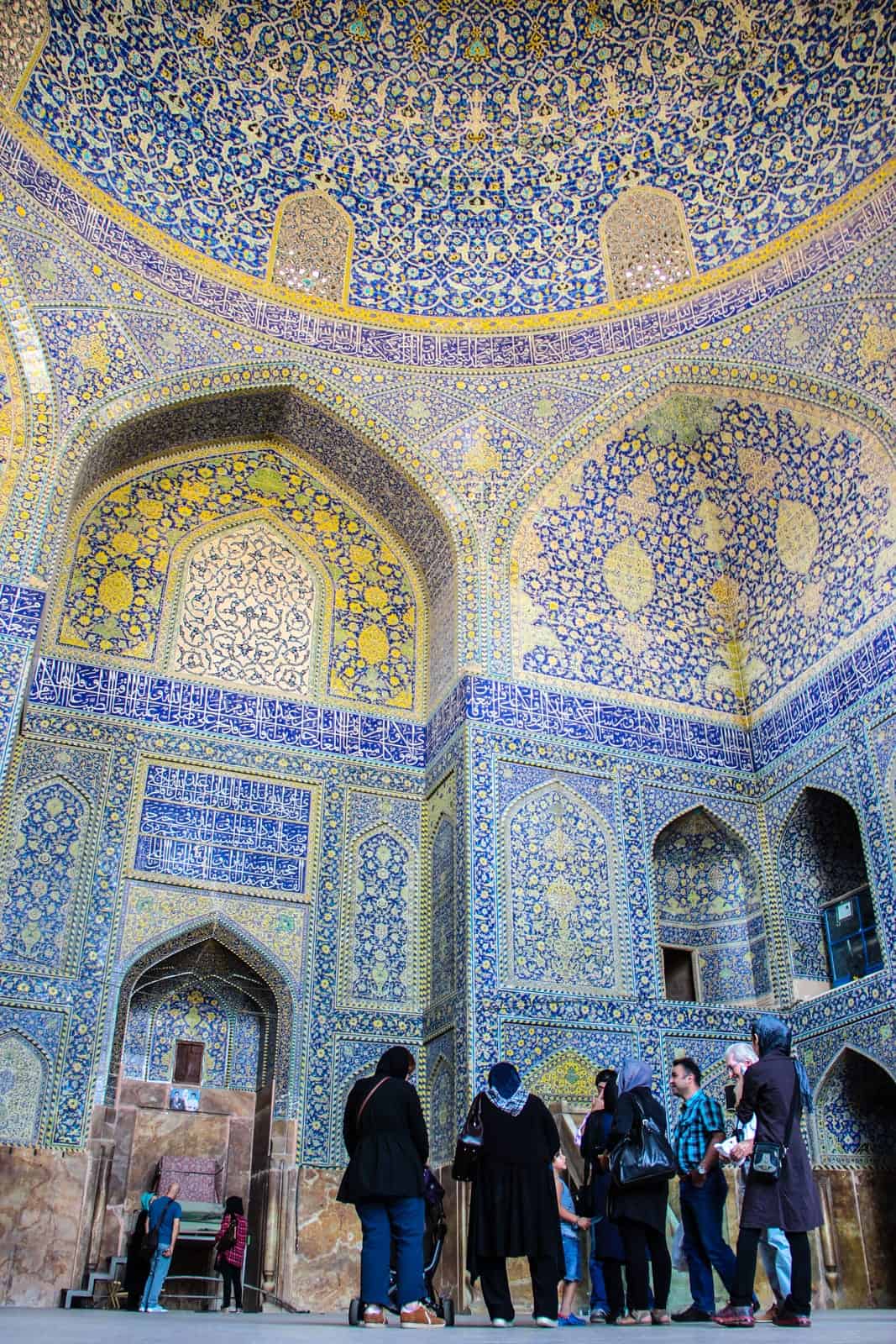 Travellers enter a mosque in Iran covered in gold and blue tiles