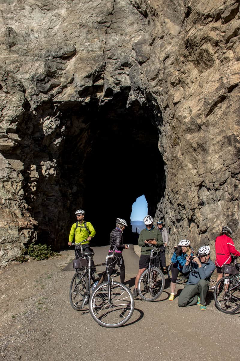 Cyclists stop for a rest and to take pictures in front of a carved-out tunnel on the Kettle Valley Rail Trail.