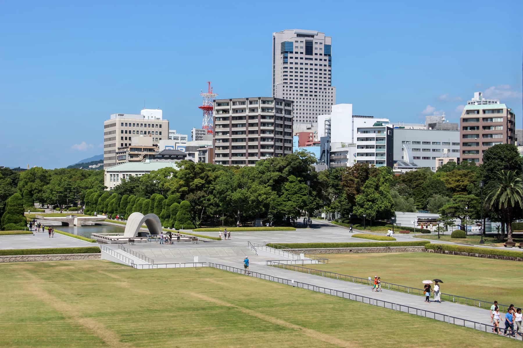 The walk ways and sculptures in the green Hiroshima Peace Park Memorial set within the modern city skyline. 