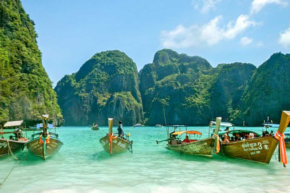 Five wooden boats lined up in the cliff-backed turquoise waters at Maya Bay in Thailand.