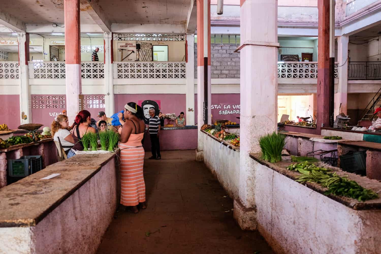 People in a pink painted market place, with a scarce amount of green produce available. 
