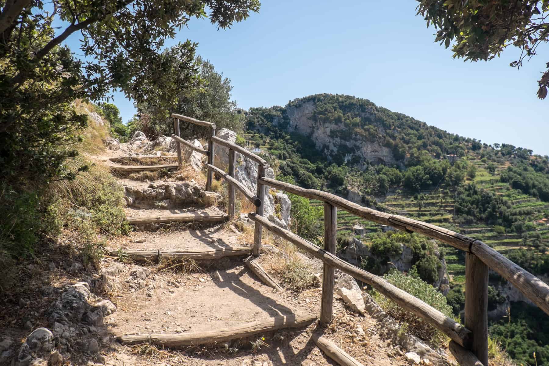 Manmade steps with wooden trims and handrails overlooking mountainous forest terraces on the Sentiero Degli Dei trail. 