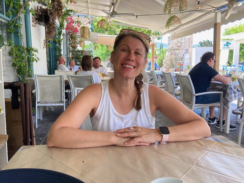 sitting at a table in greece, smiling but with pain underneath
