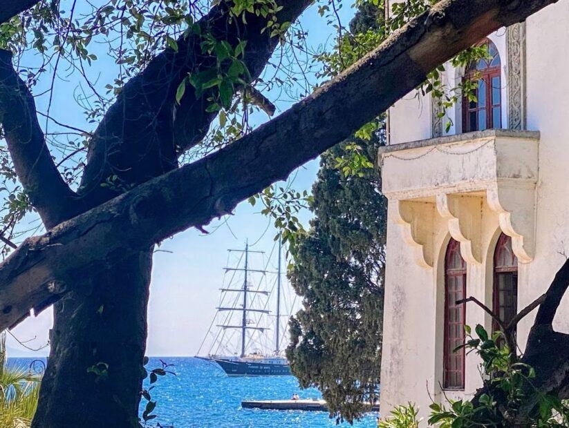 View of Running on Waves cruise seen from between a tree and old building on Kos Island