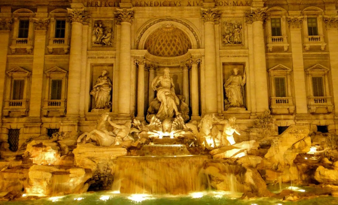 trevi fountain at night lit in golden glow