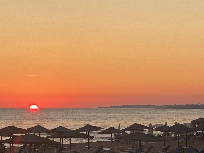 Orange sunset on the beach with thatched beach umbrellas in Corfu Greece