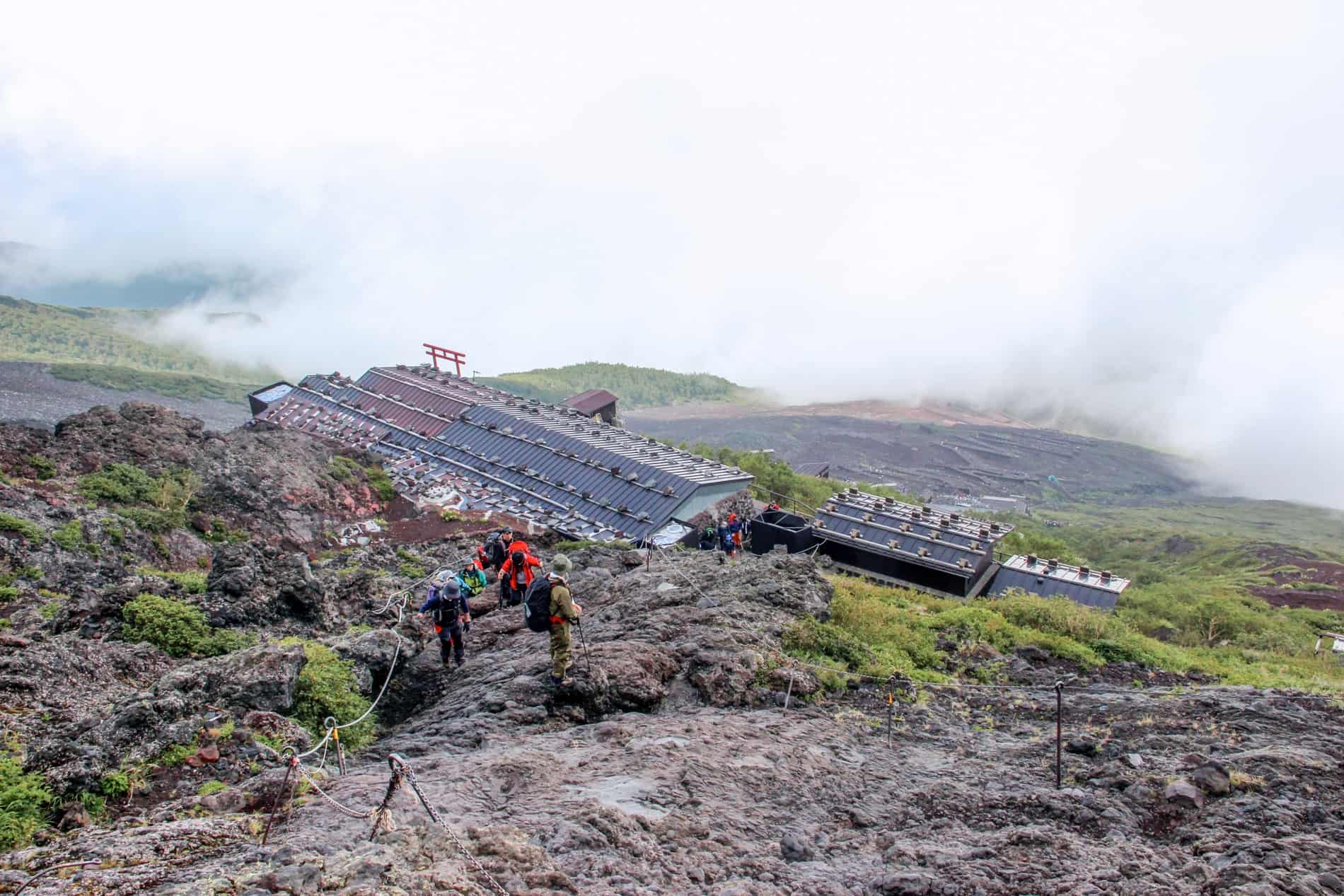 Hikers walking over a huge rocky mound above a mountain hut on Mount Fuji. 