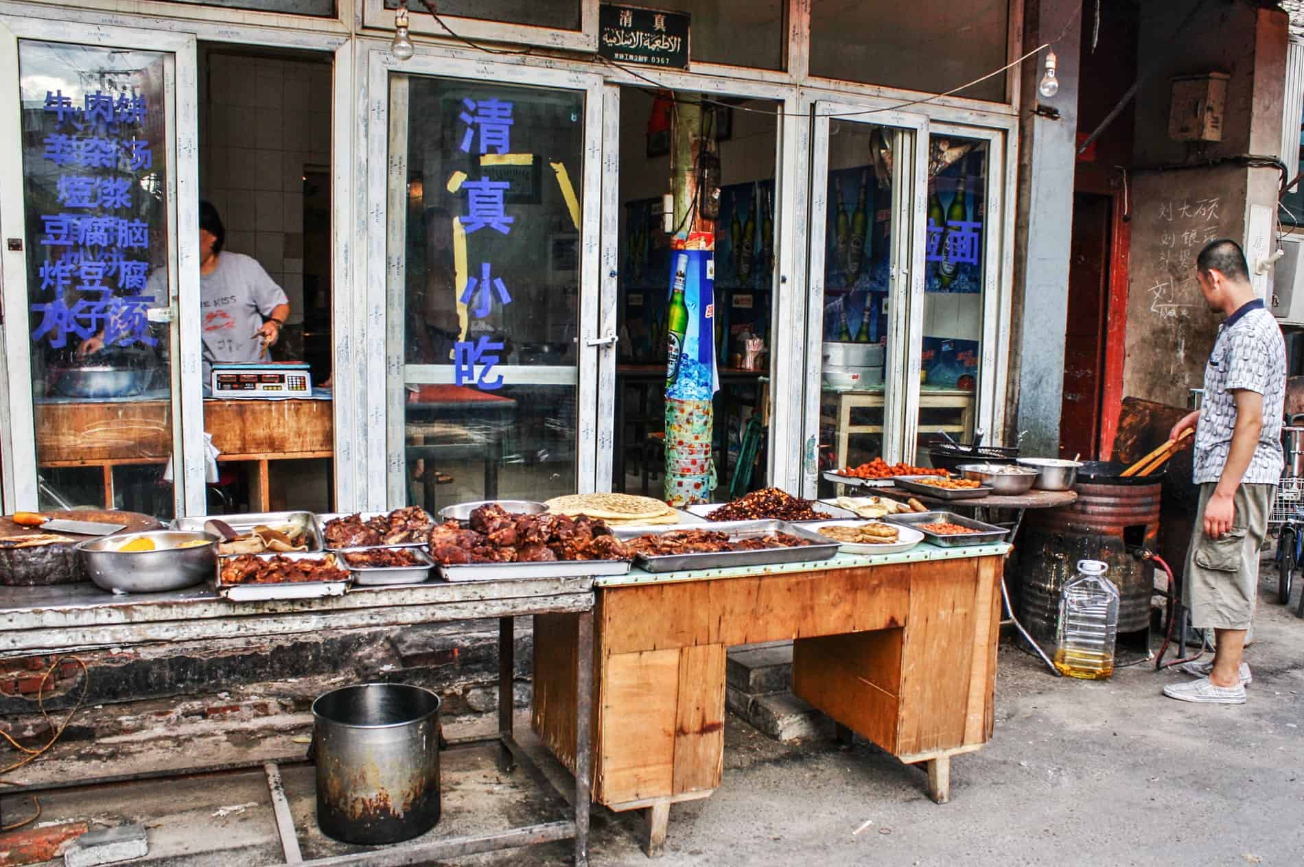 A man standing at a grill need to a long table of cooked meats . 