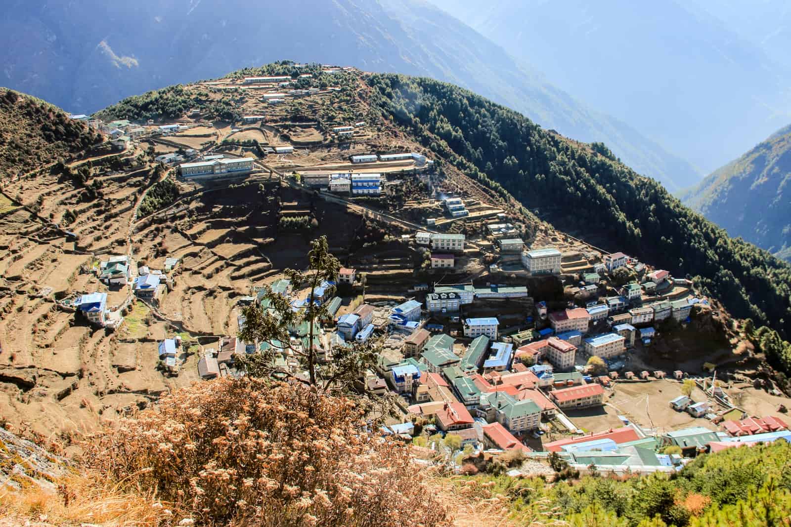 An elevated view of Namche Bazaar on the Everest Base Camp Trek - a collection of teahouses and small buildings nestled on a tiered landscape in a mountain valley