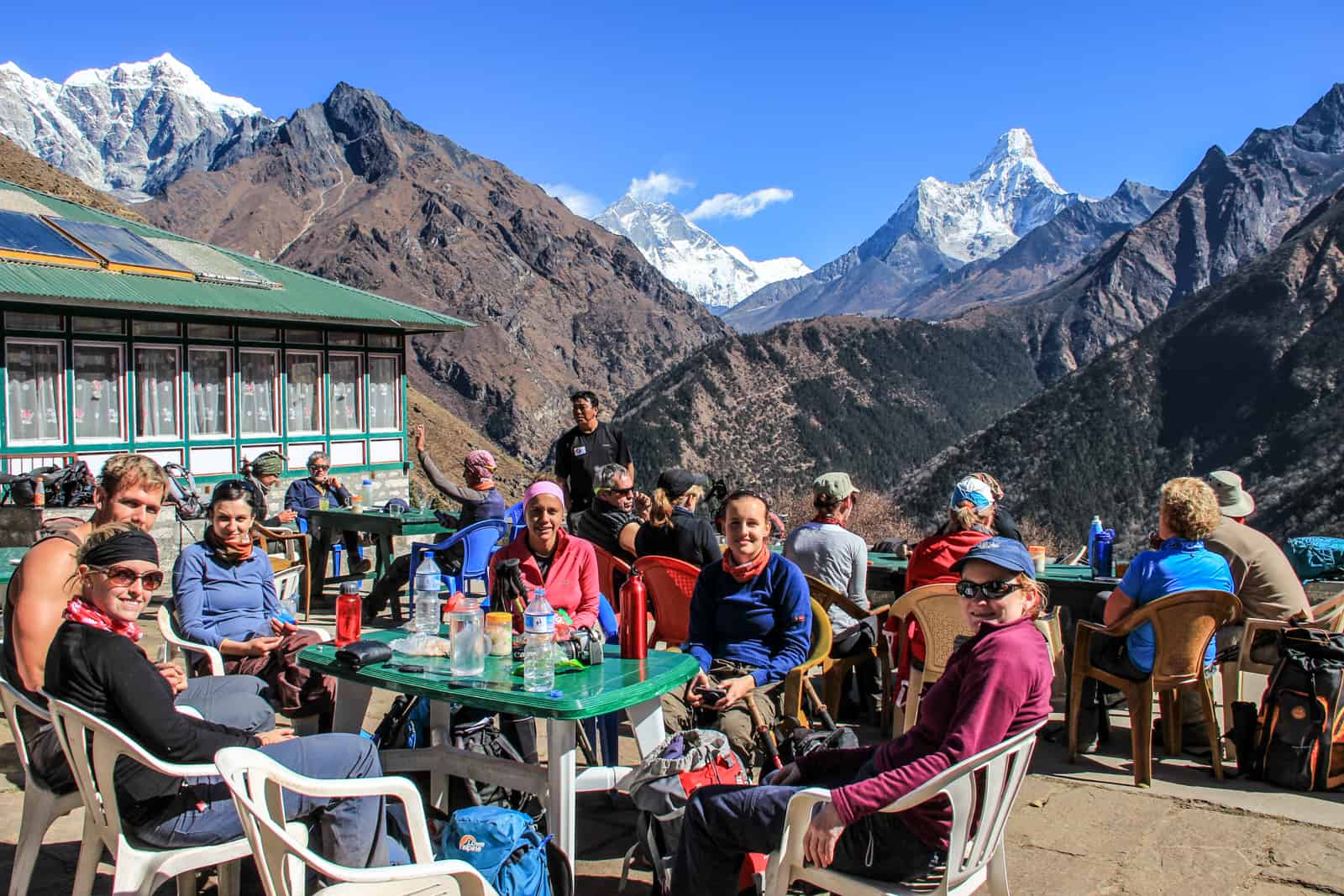 A small group of trekkers gathered around a table outside a green Nepalese tea house, backed by high mountain vistas – a typical rest stop on the Everest Base Camp trek