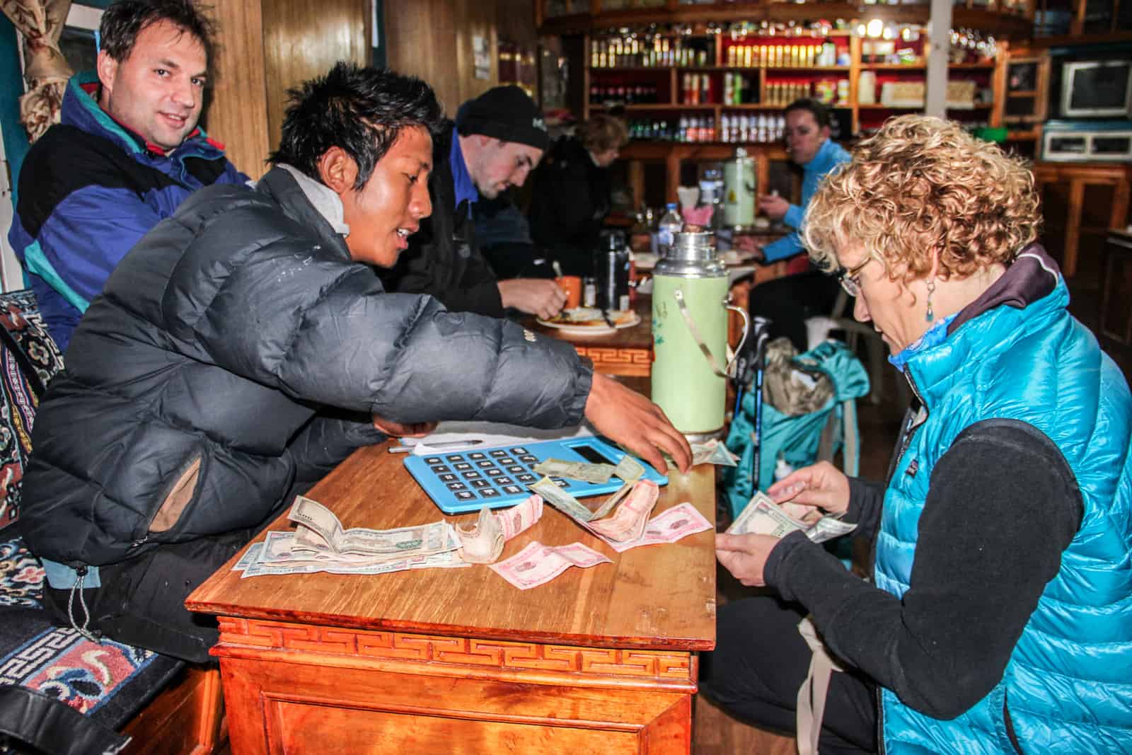 A Nepalese porter exchanges money with a female trekker on a wooden table in a traditional wooden teahouse on the EBC Trek