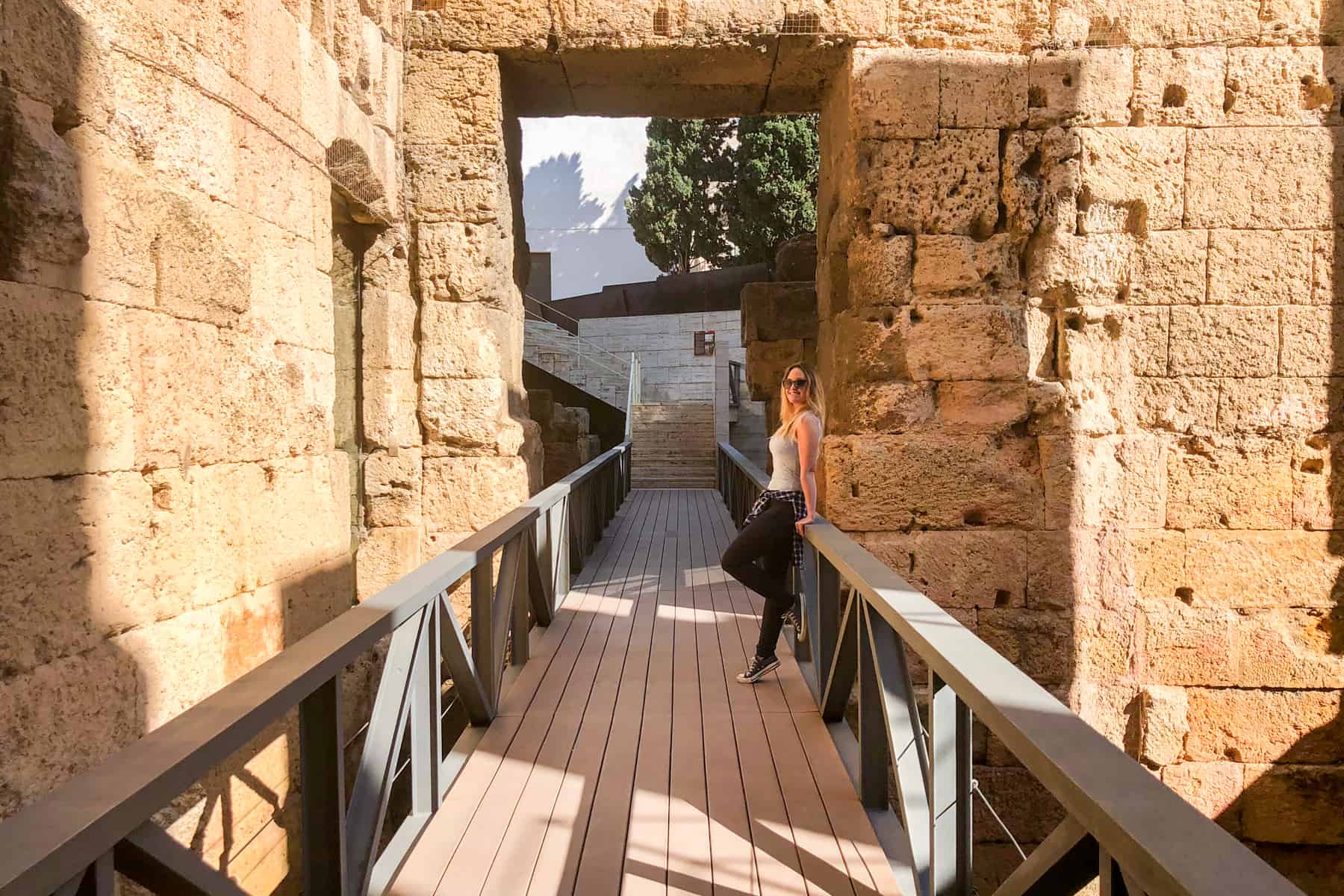 A woman leans on a wooden barriers in a golden stone square doorway, inside the Roman Circus of Tarragona Spain 