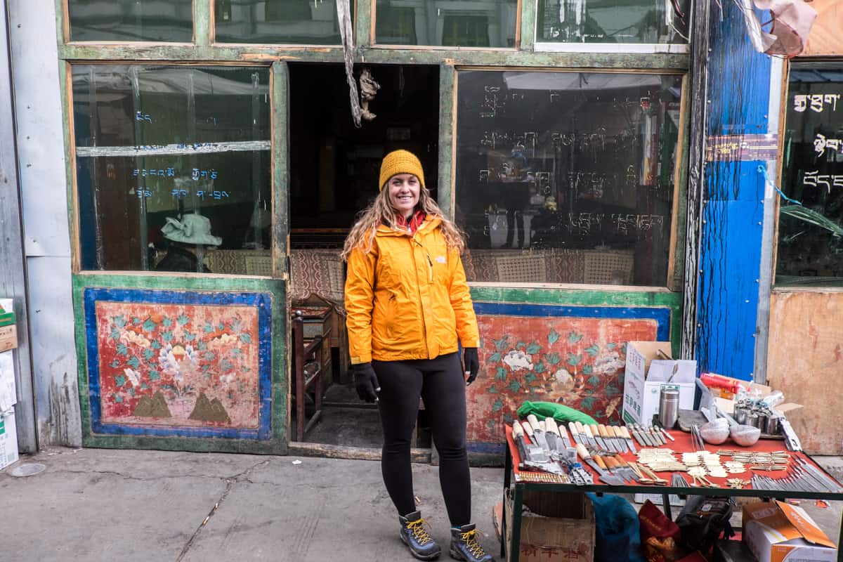 A woman wearing orange stands outside a traditional teahouse in a Tibetan market in Gyanstse during travel in Tibet