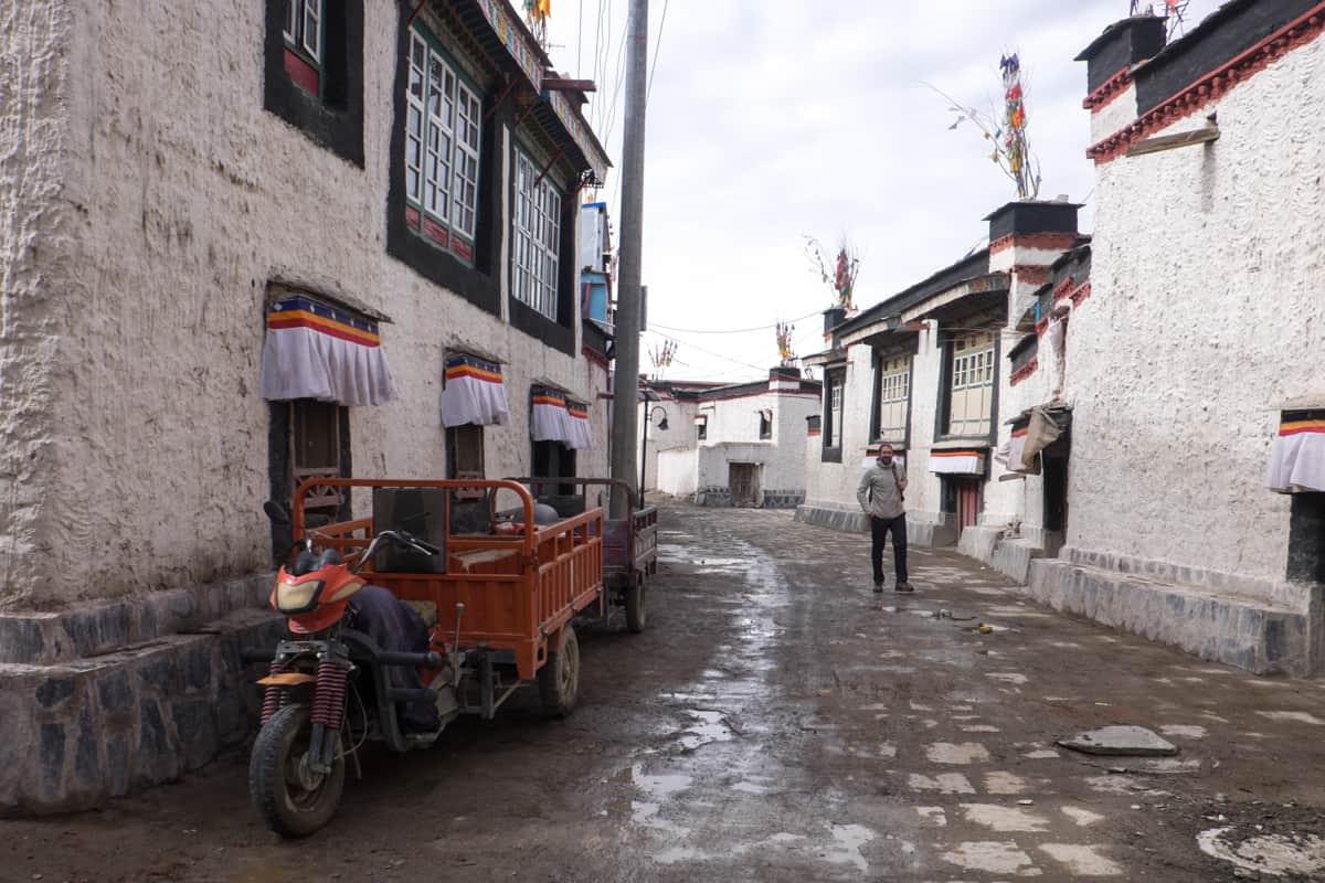 Male tourist walks in the quiet and traditional village in Gyantse filled with white Tibetan houses with black trimmed windows