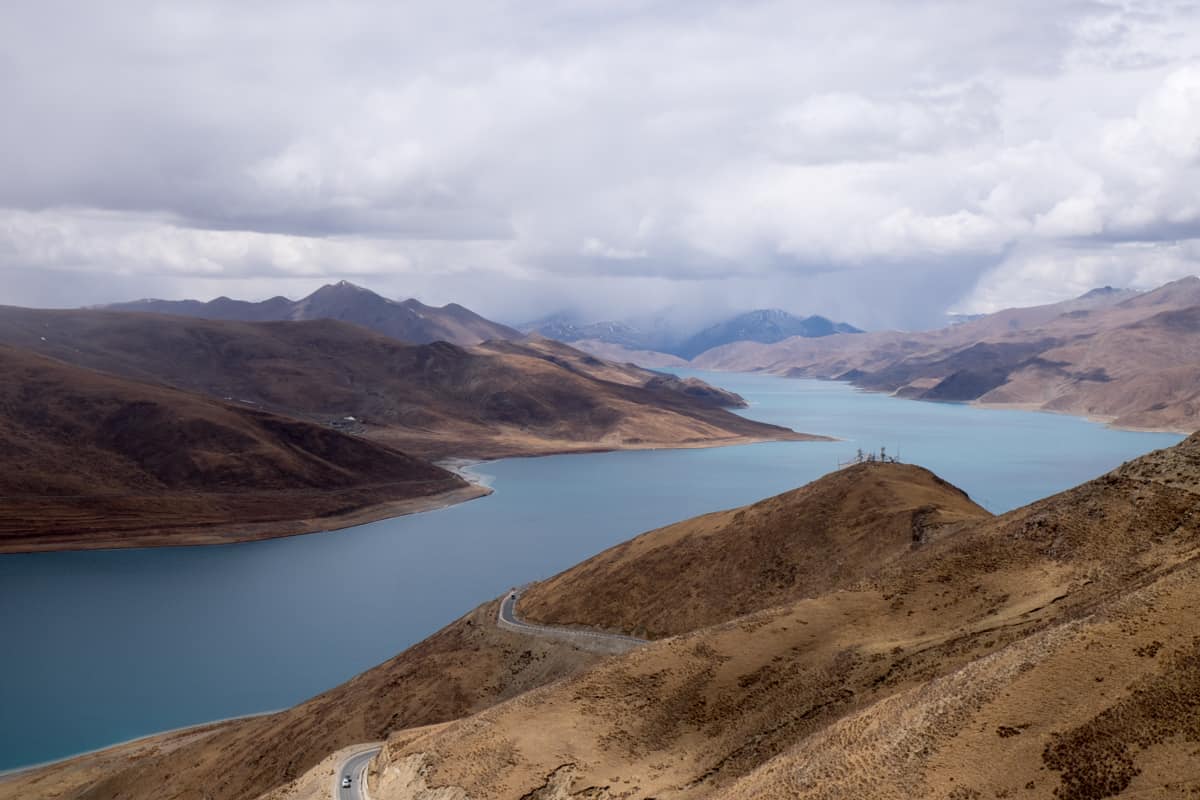 Overland travel in Tibet passes the biggest lake in the country, the aqua blue Yamdork lake, surrounded by dry mountainous land