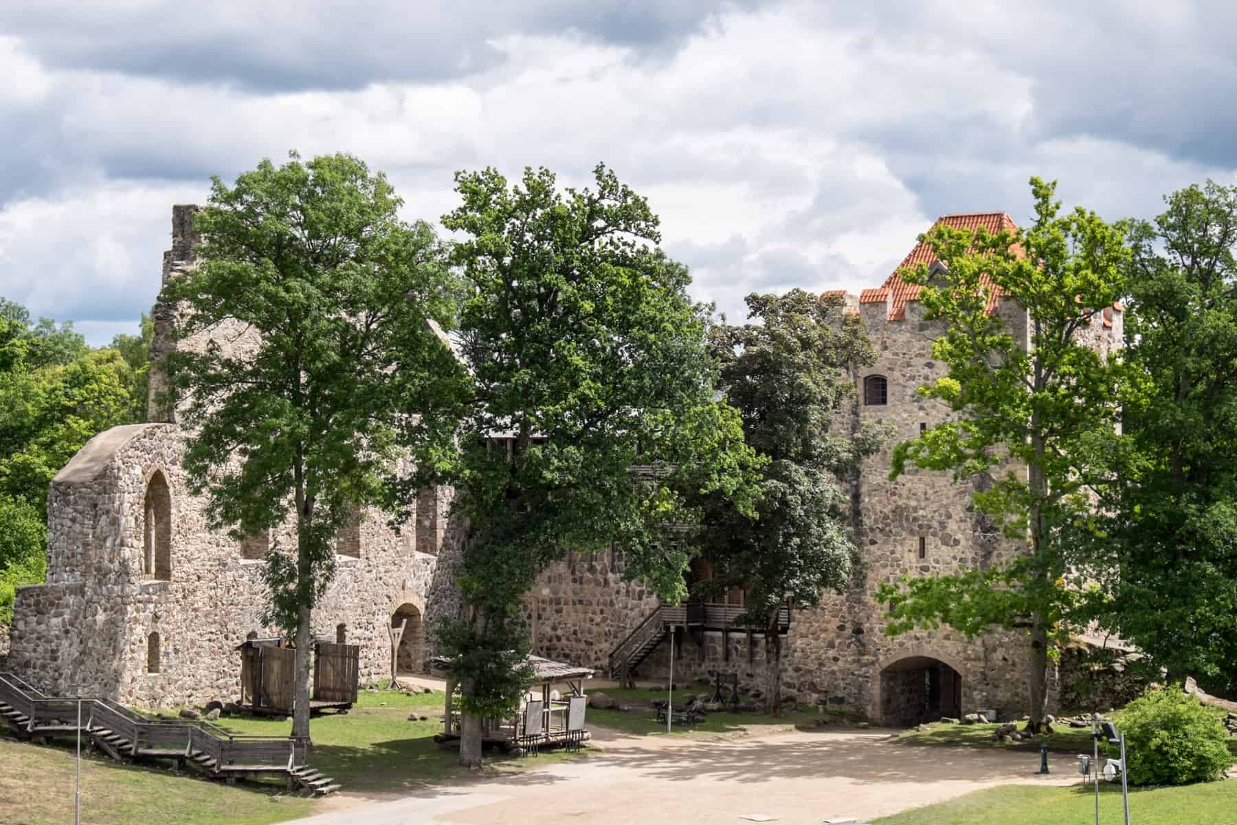 The beige ruins of a Latvian medieval castle with an orange roof can be seen behind five trees