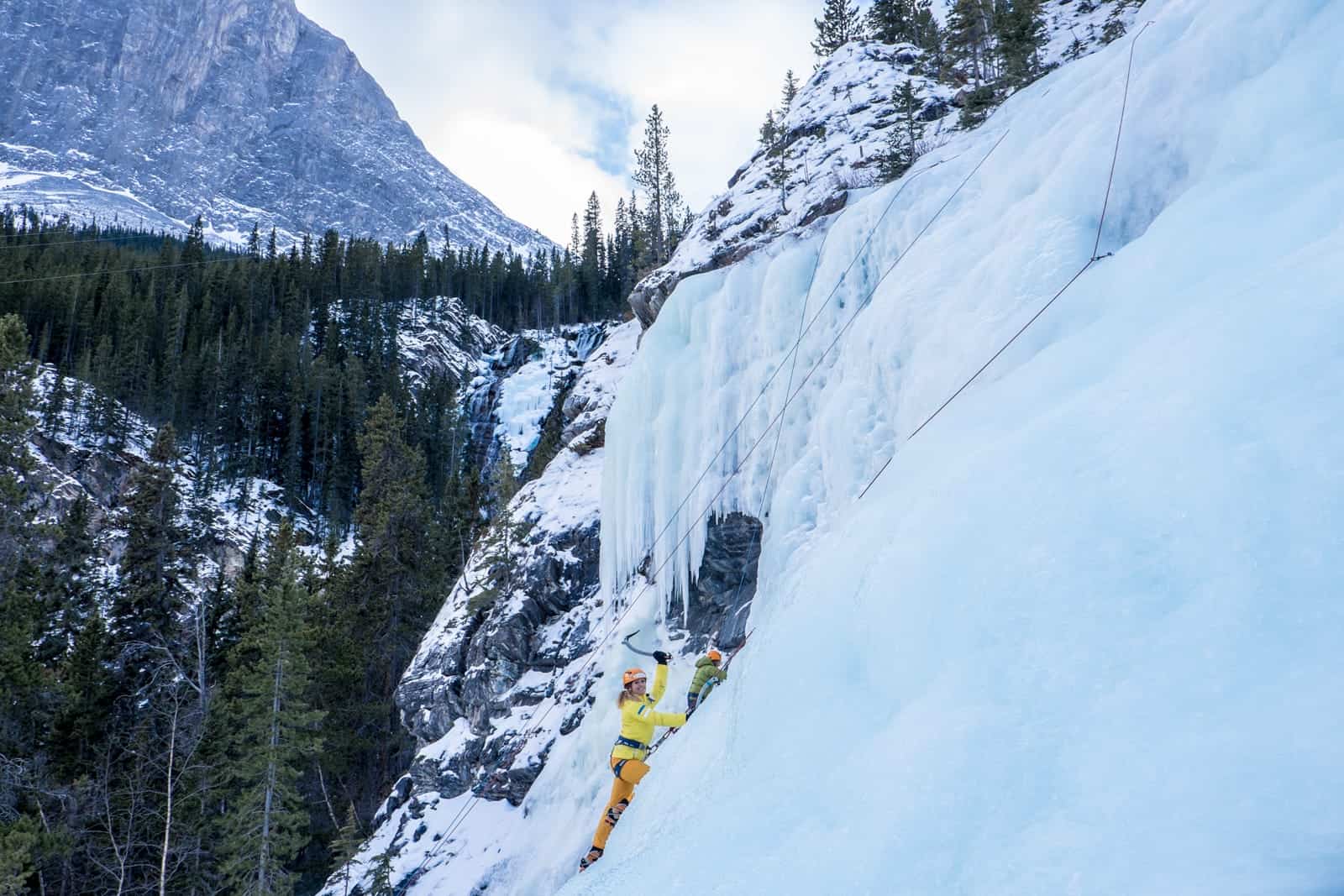 Woman ice climbing a frozen waterfall in winter in Banff 