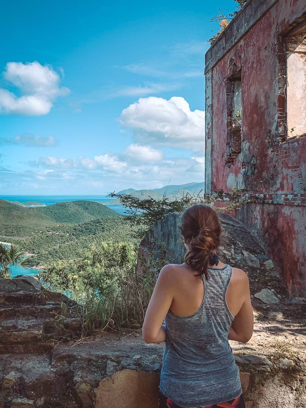 brunette girl in tank top next to plantation ruin overlooking Maho Bay