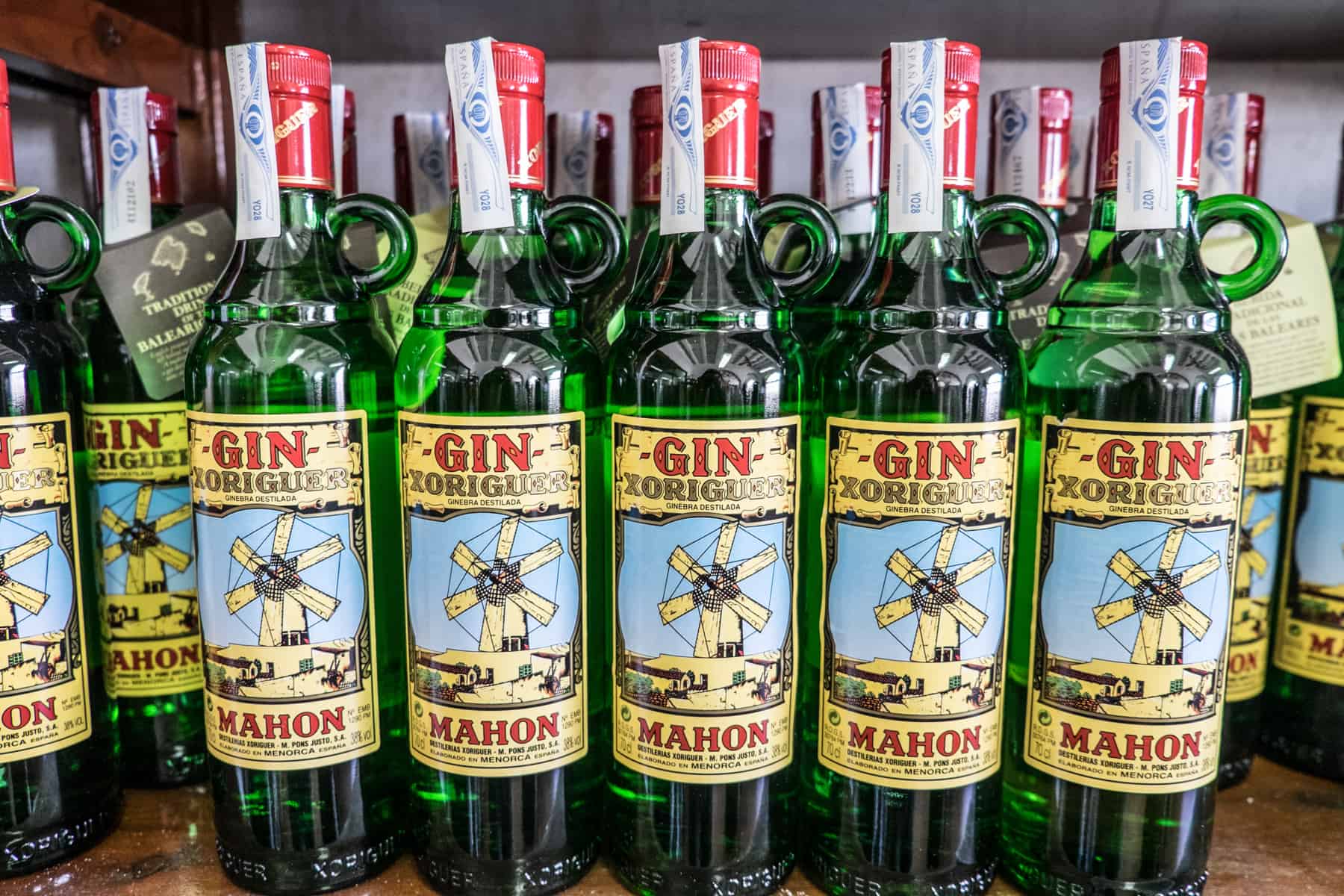 Rows of Menorca's famed Mahon Xoriguer Gin in green bottles with a yellow label and red lid. 