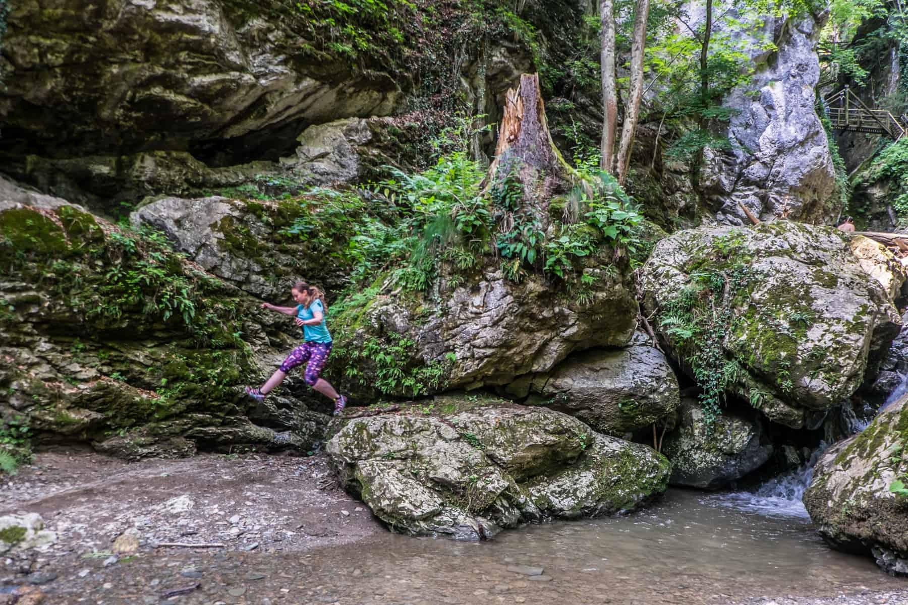 A woman jumps off a large rock in a woodland canyon in Graz Austria
