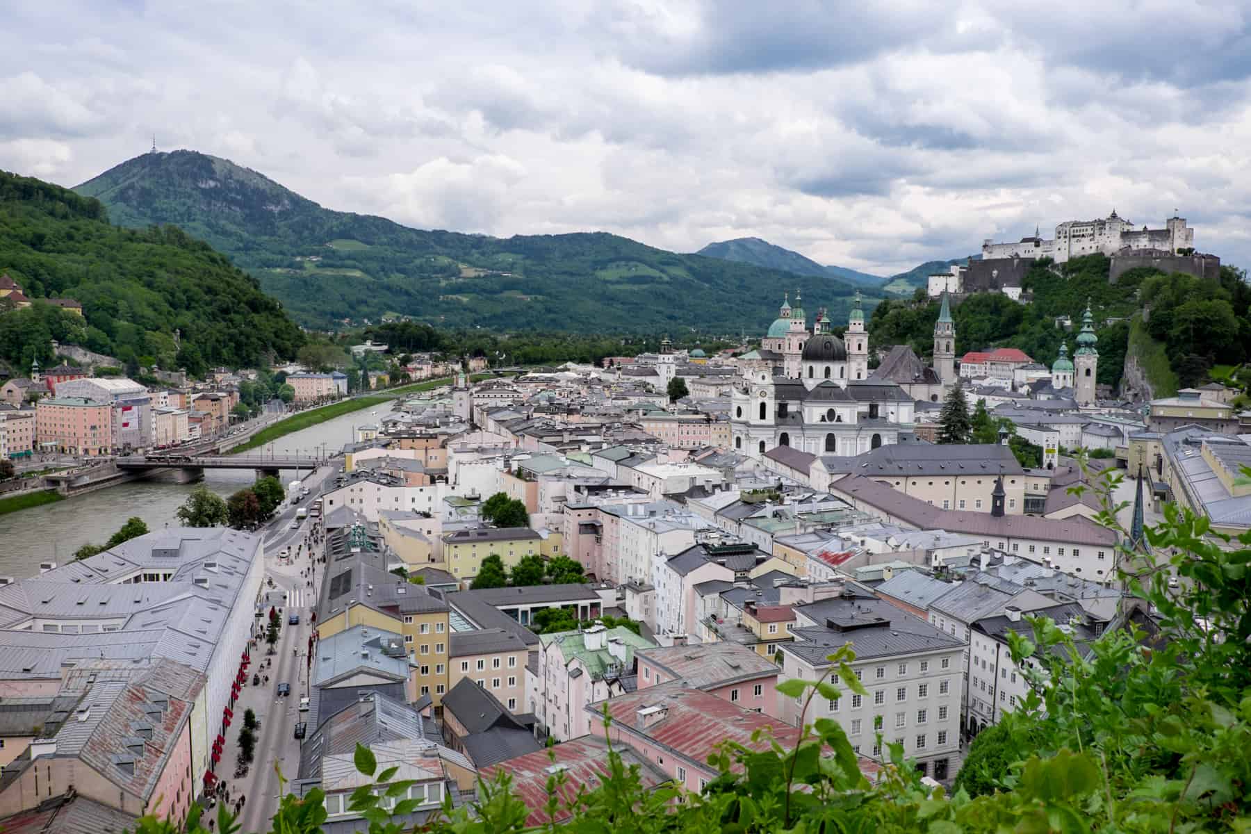 Arial view of the riverside Salzburg Historical Old Town with it pastel buildings, mint green rooftops and castle on the hill.