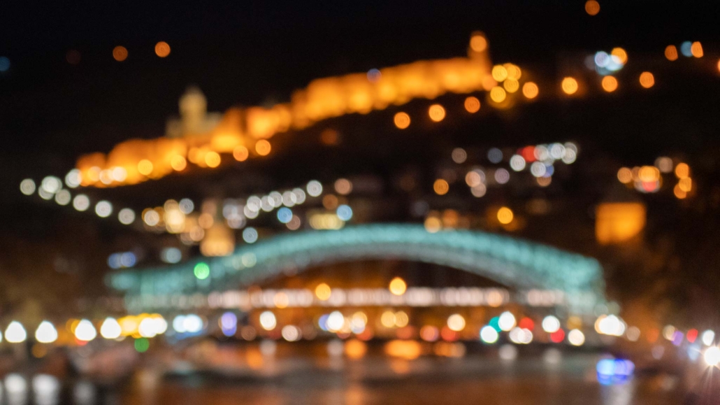 A blurry shot of Tbilisi at night, with the light and shape of the fortress and river bridge