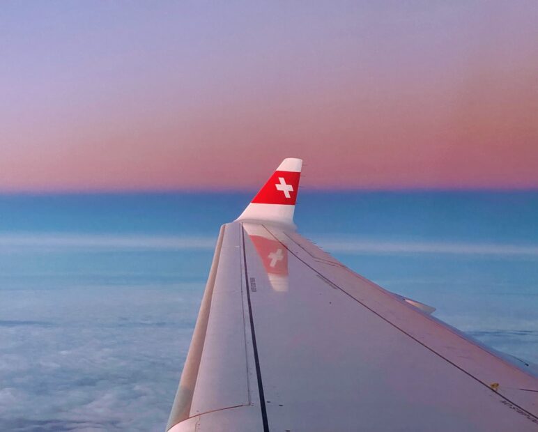 Wing of Swiss air plane with logo in the sky during sunset