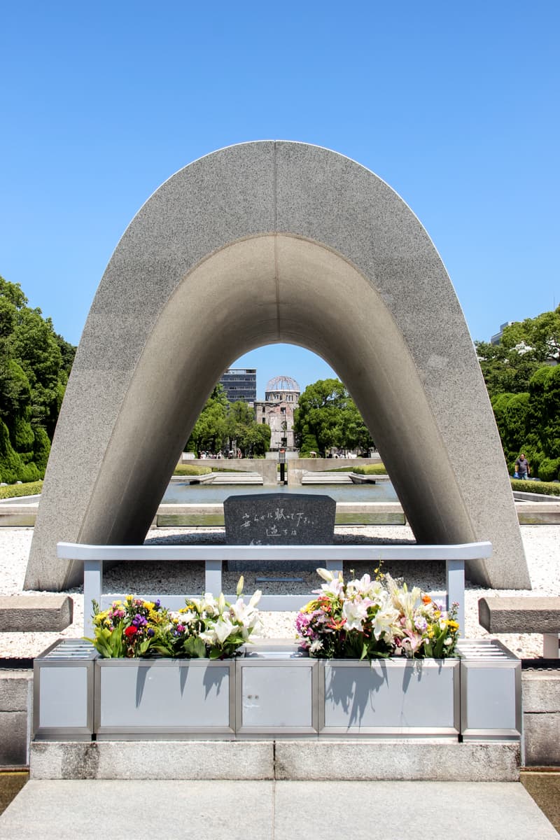 A stone archway sculpture that looks towards the the Flame of Peace and the A-Bomb Done in Hiroshima Peace Park Memorial. 