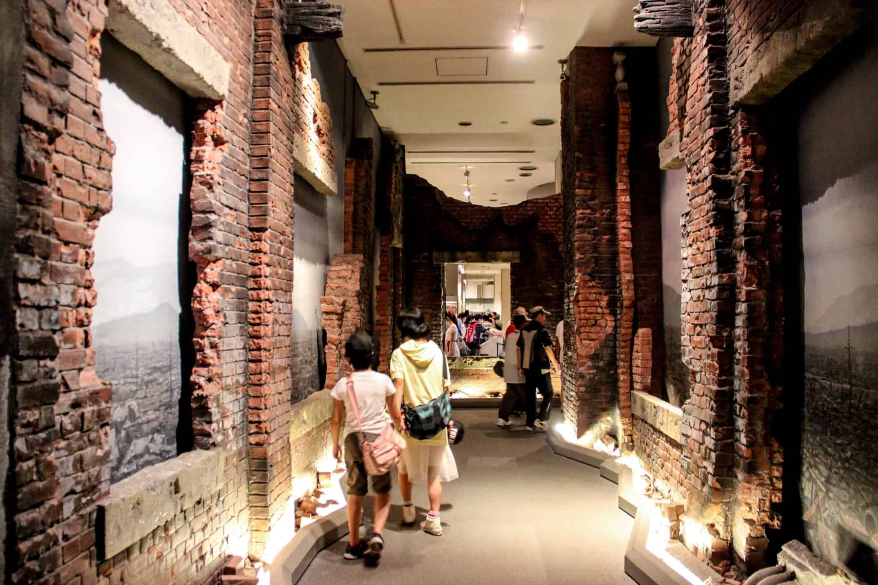 An exhibit inside Hiroshima Peace Memorial Museum showing crumbling brick walls and black and white images. 