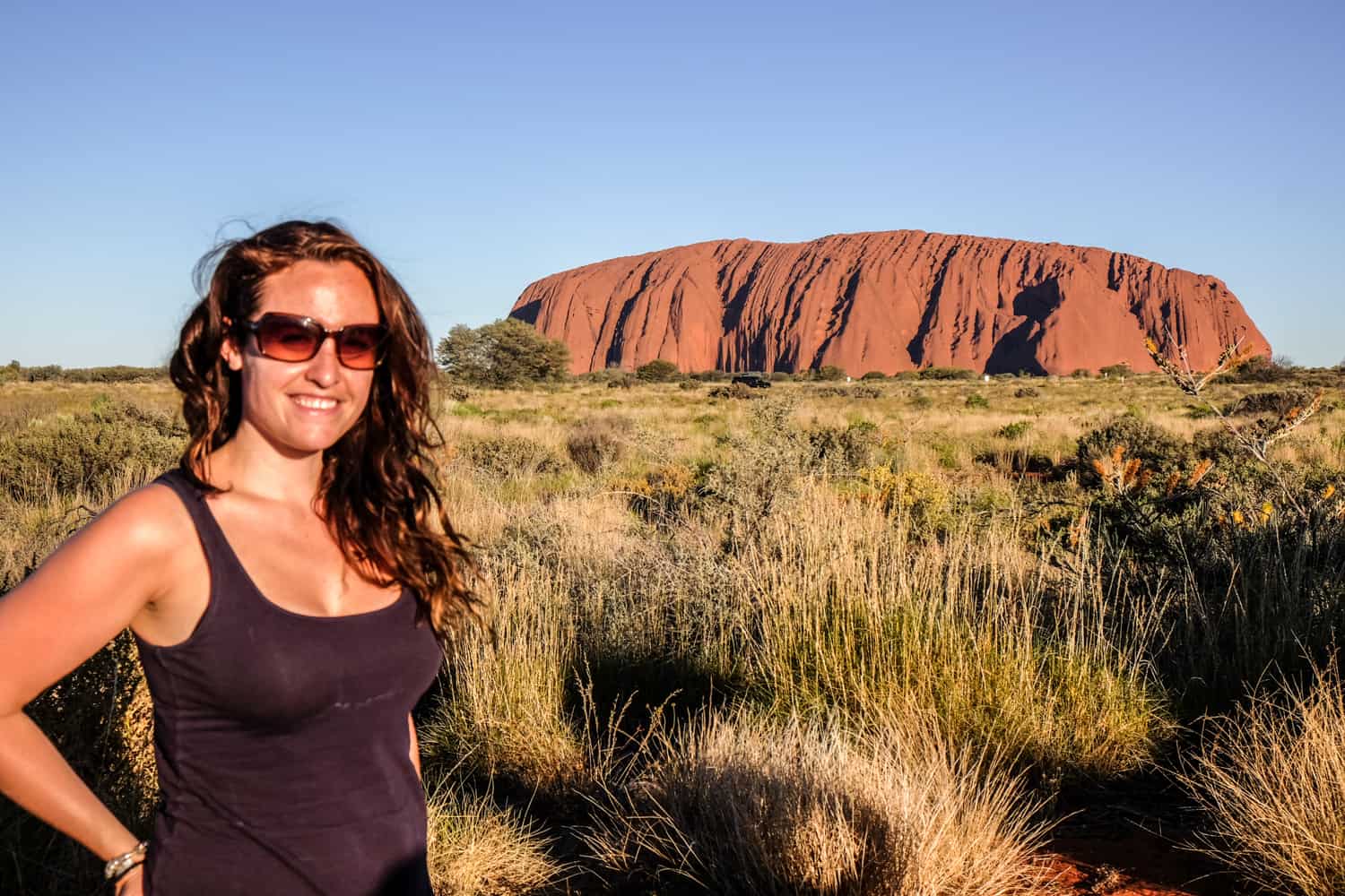A woman standing in front of Uluru at sunset. 