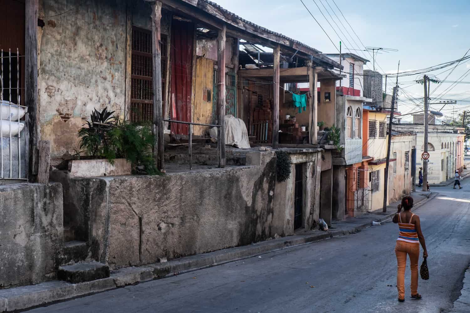 A woman walks down a neighbourhood street with low rise, run-down buildings in Cuba. 