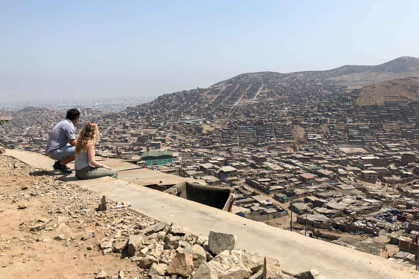 A Peruvian tour guide and a tourist sit at a stone ledge looking out over the San Juan barrio of Lima, Peru.