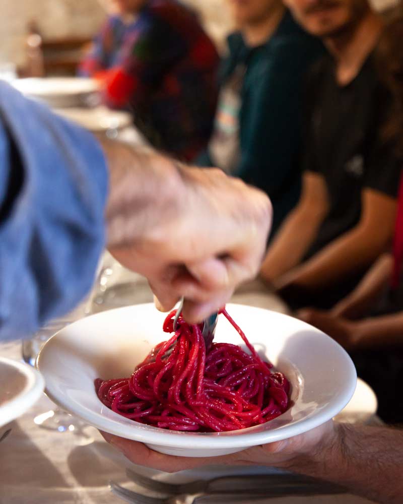 A plate of purple pasta, coloured from the beetroot it is boiled with, is dished out by the waiter
