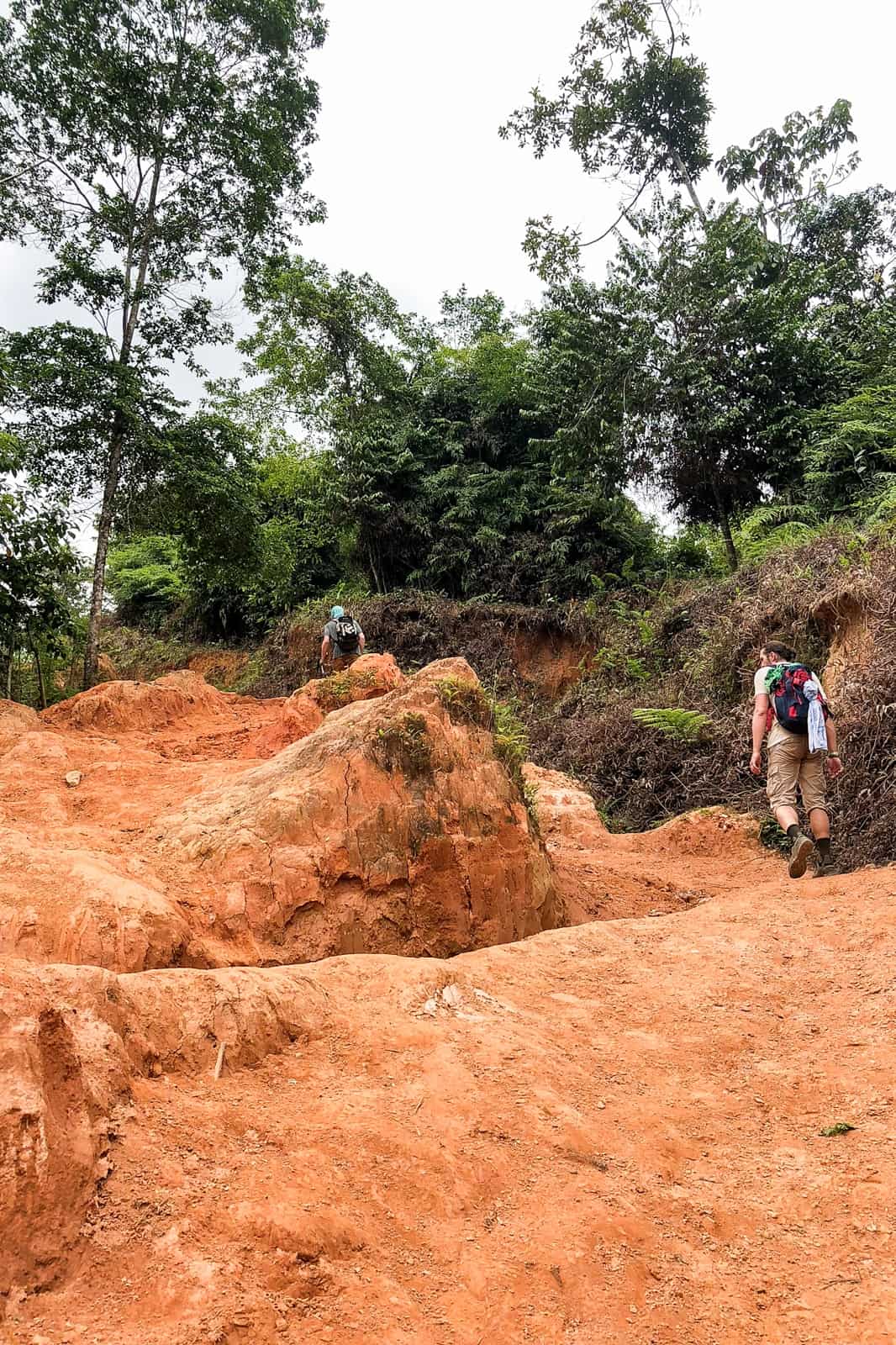 Two men trekking on steep, orange mud trails on the Lost City trek in Colombia.