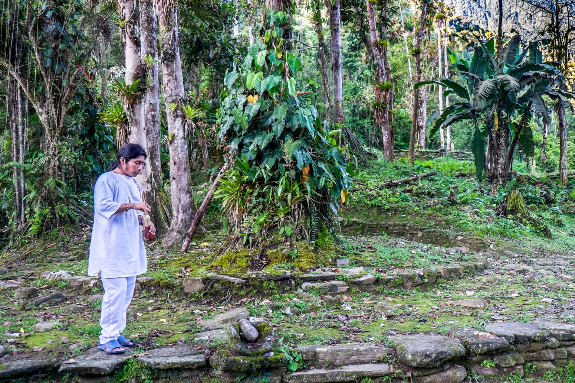 Wiwa man in white dress standing within the jungle stone ruins of The Lost City Ciudad Perdida in Colombia.
